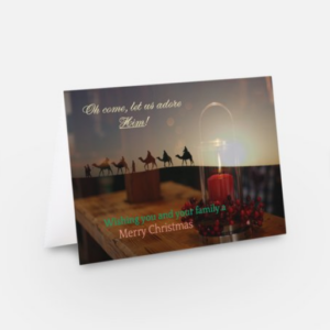 Front of Christmas greeting card with a picture of a red candle on a table overlaid with the image of a line of camels against the sun, and overlaid with the texts "Oh come let us adore Him" and "Wishing you and your family a Merry Christmas".